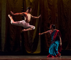 Dancer on left jumps in a stag, right dancer crouches down.