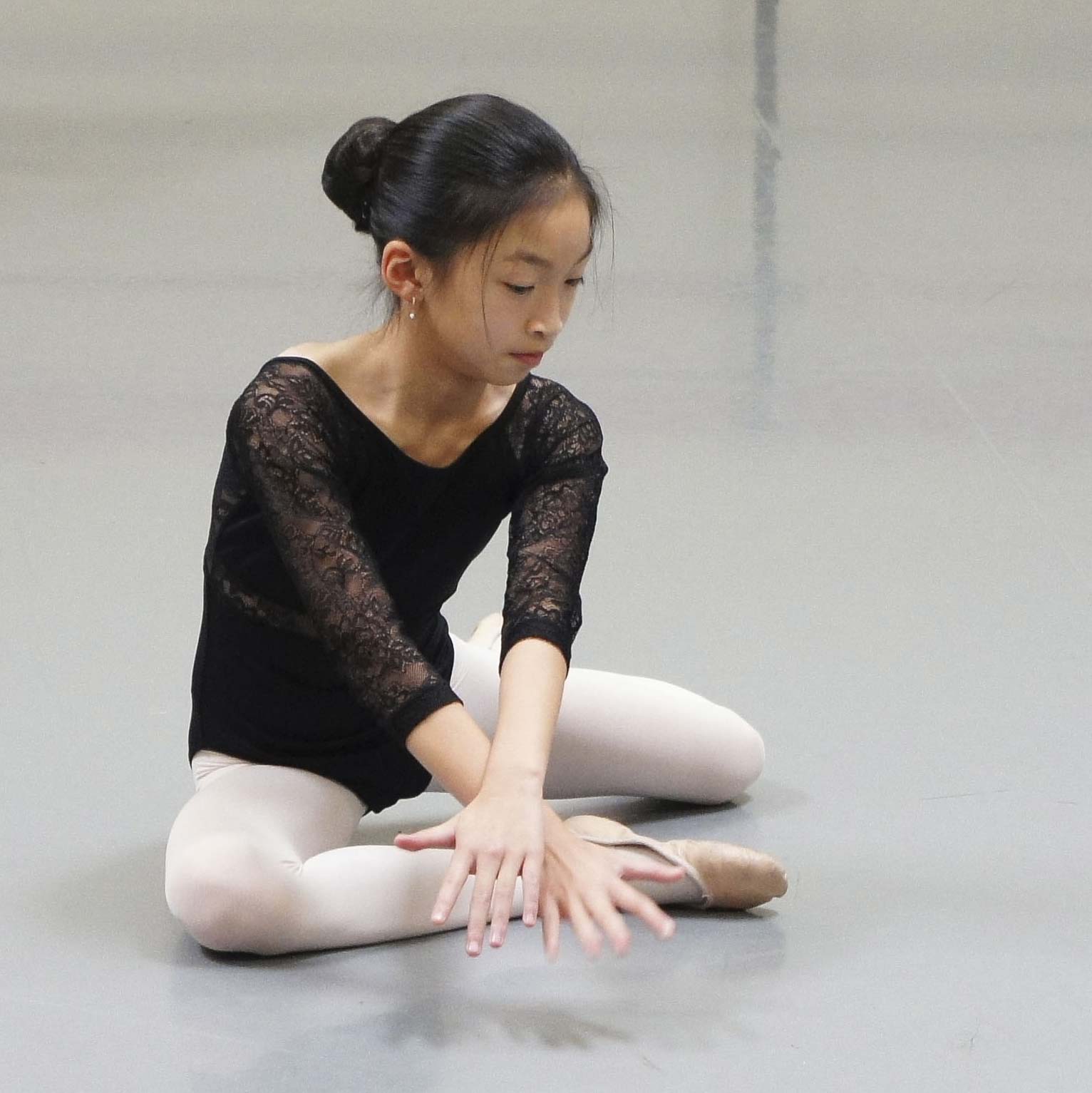 Ballet dancer sitting on floor with hands crossed in front