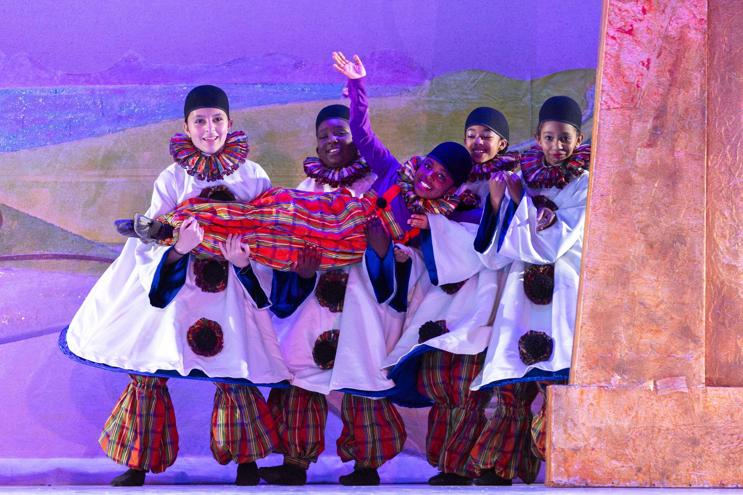 Nutcracker students in white costumes holding another student laying across them and waving.